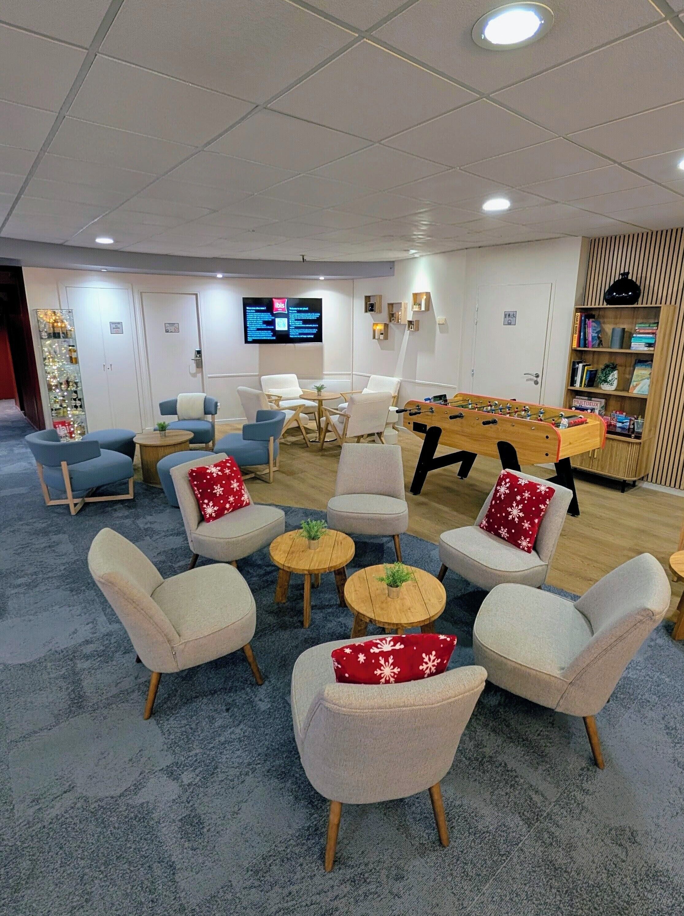 A modern lounge area with sofas, a foosball table, and a TV screen displaying information.