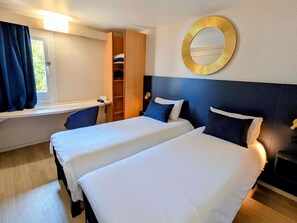 A hotel room with two beds, a large mirror, a window with curtains, a wooden wardrobe, and a desk with a phone. - Ibis Grenoble Centre Bastille (Grenoble)