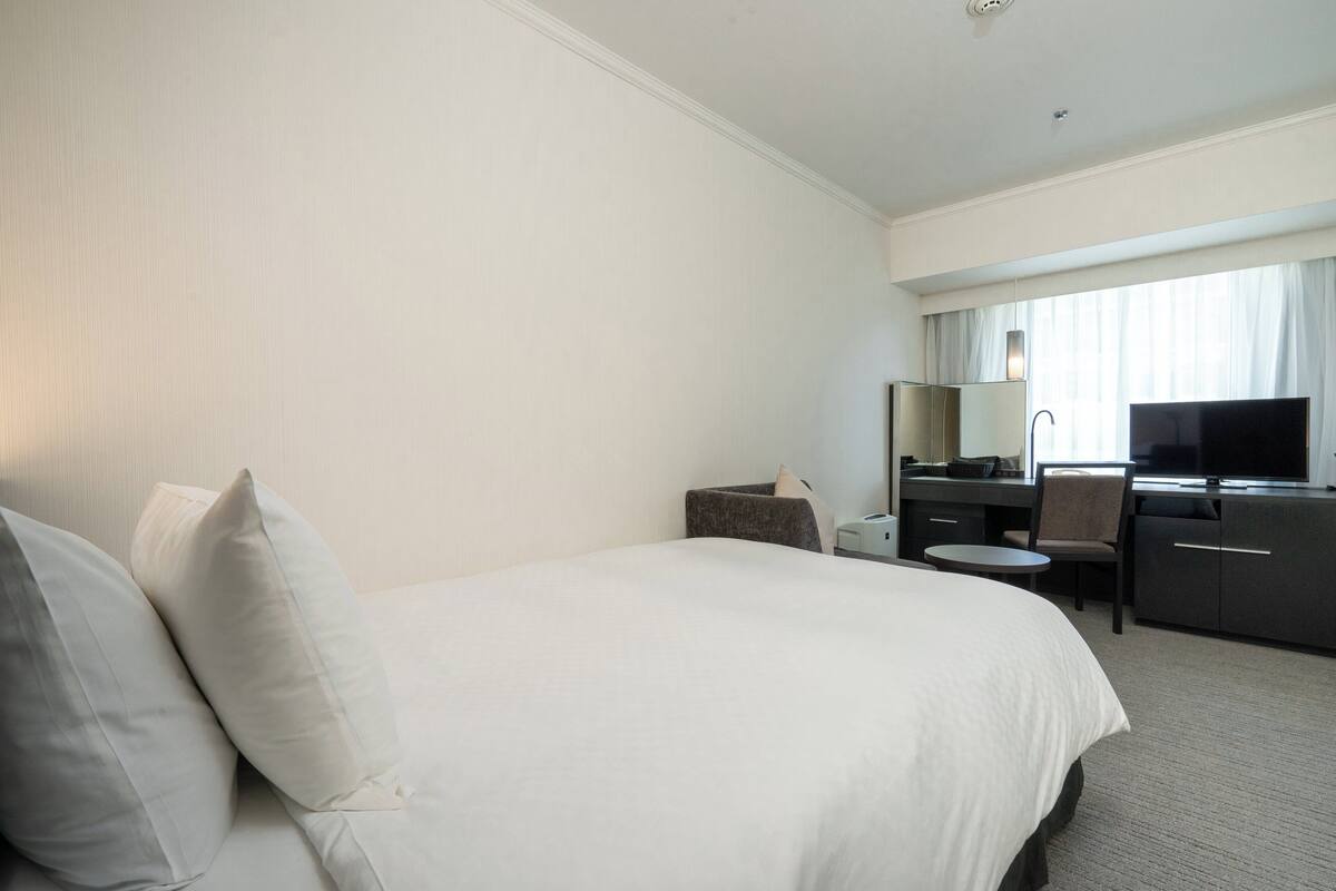 A hotel room with a large bed, a desk, a chair, a television, and a window with curtains.