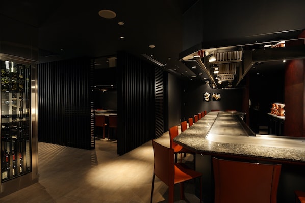 A modern bar area with a long counter, multiple seating options, and a visible wine rack.