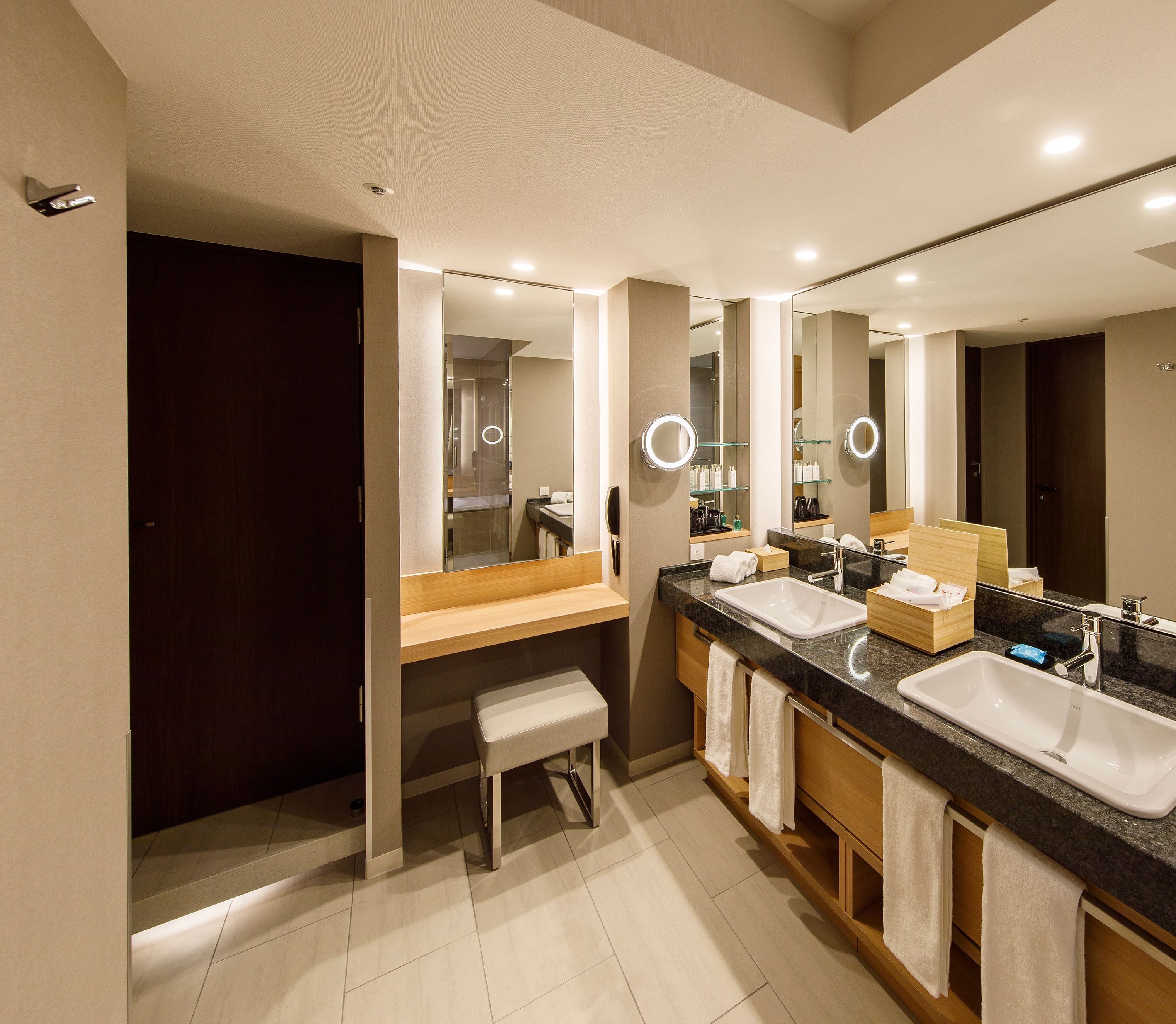 Un baño moderno con dos lavamanos, un banco y un espejo grande.