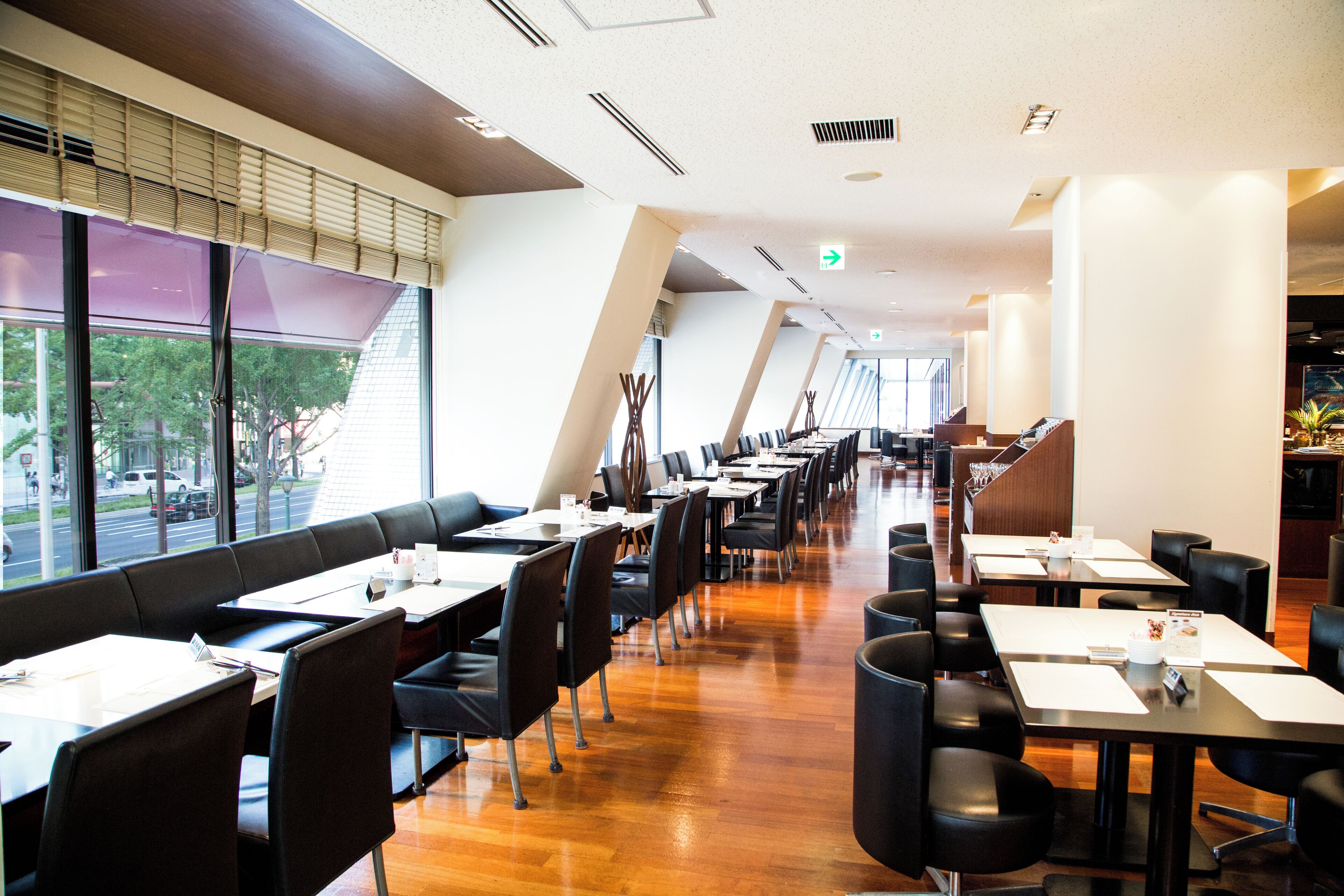 Ein modernes Restaurant mit langen Tischen und Sitzecken, großen Fenstern und Holzboden.