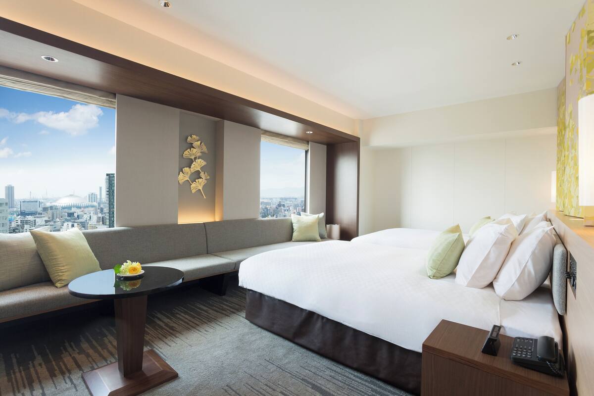 A modern hotel room with a large bed, a sofa, a small table, and a city view.
