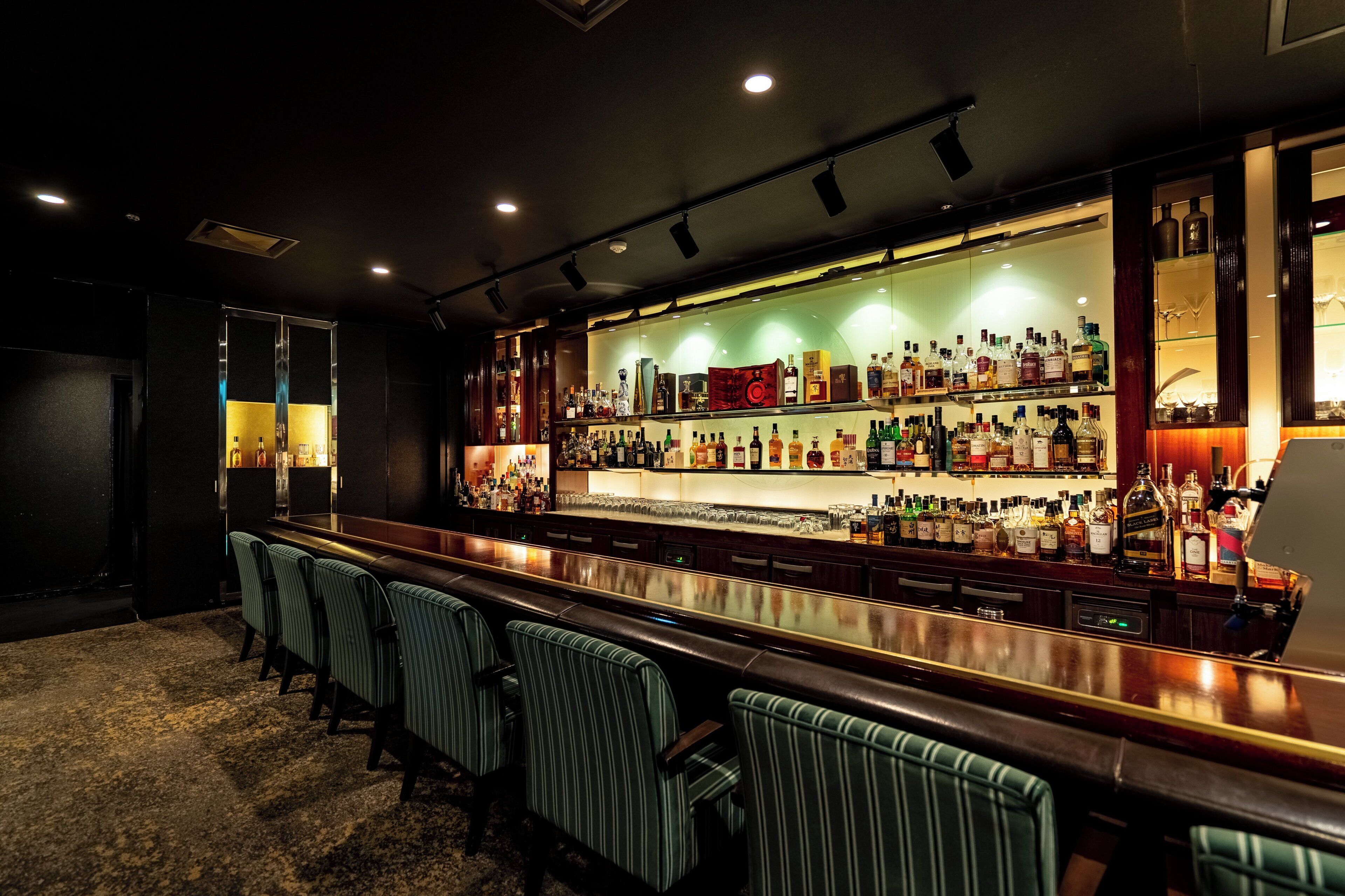 A bar area with a long counter, multiple shelves of bottles, and striped bar stools.