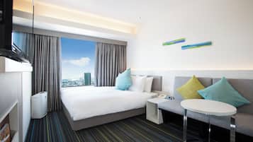 Una habitación de hotel con una cama grande, un sofá, una mesita y vistas a la ciudad.