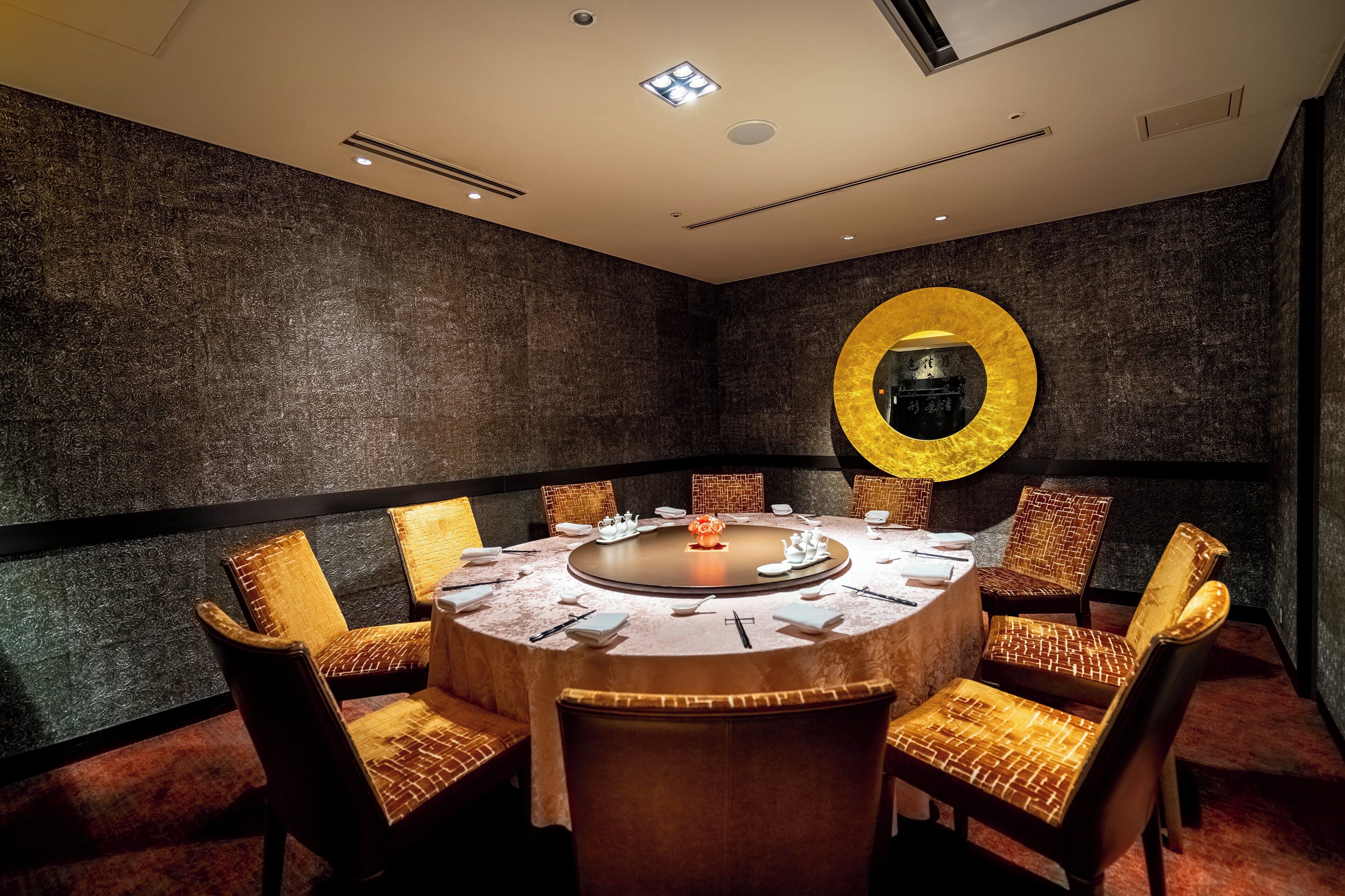 A conference room with a round table, chairs, and a large mirror on the wall.