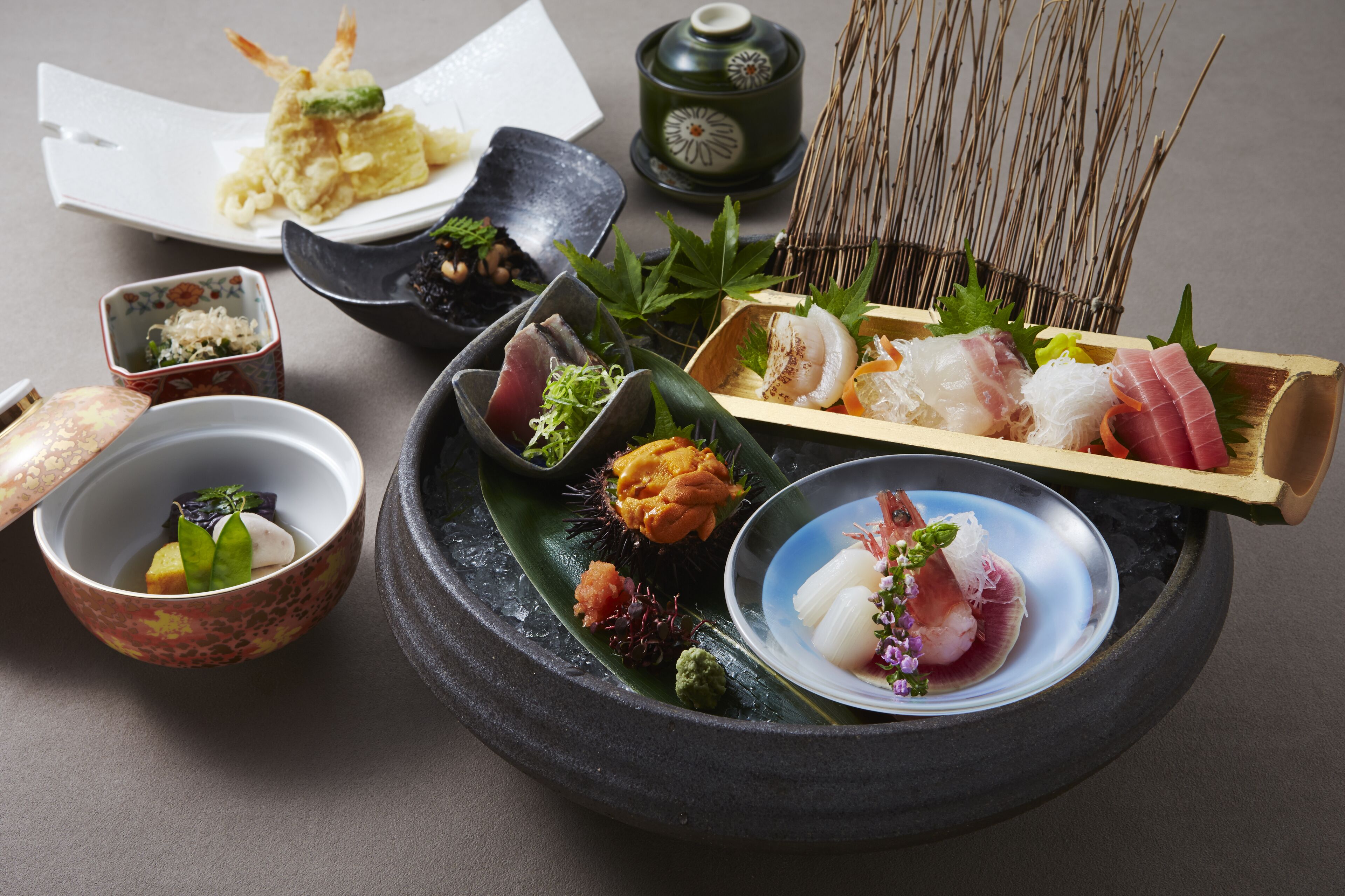 Variedad de platos japoneses, como sushi, sashimi y tempura, dispuestos sobre una bandeja negra con una hoja verde.
