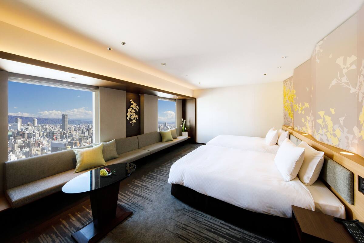 A hotel room with a large bed, a sofa, a desk, and a view of a cityscape.