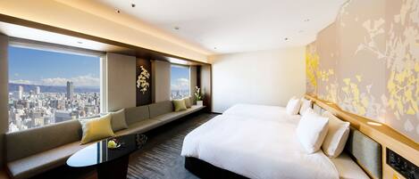A hotel room with a large bed, a sofa, a desk, and a view of a cityscape.