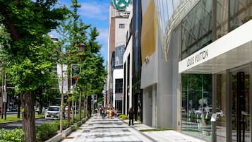 Una calle urbana moderna con una tienda Louis Vuitton, una farmacia y una acera bordeada de árboles.