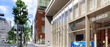 Vista de una calle con comercios, incluyendo Fendi y Hermès, un paso de peatones y una acera bordeada de árboles.