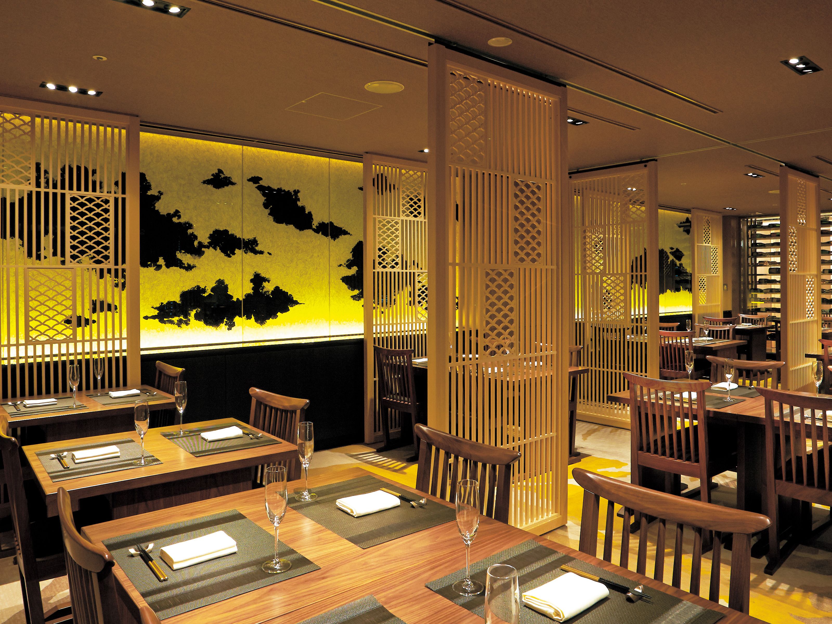 A restaurant with wooden tables and chairs, some with wine glasses and napkins.