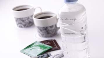 A bottle of water, two cups of coffee, and some chocolate and tea packets on a white surface.