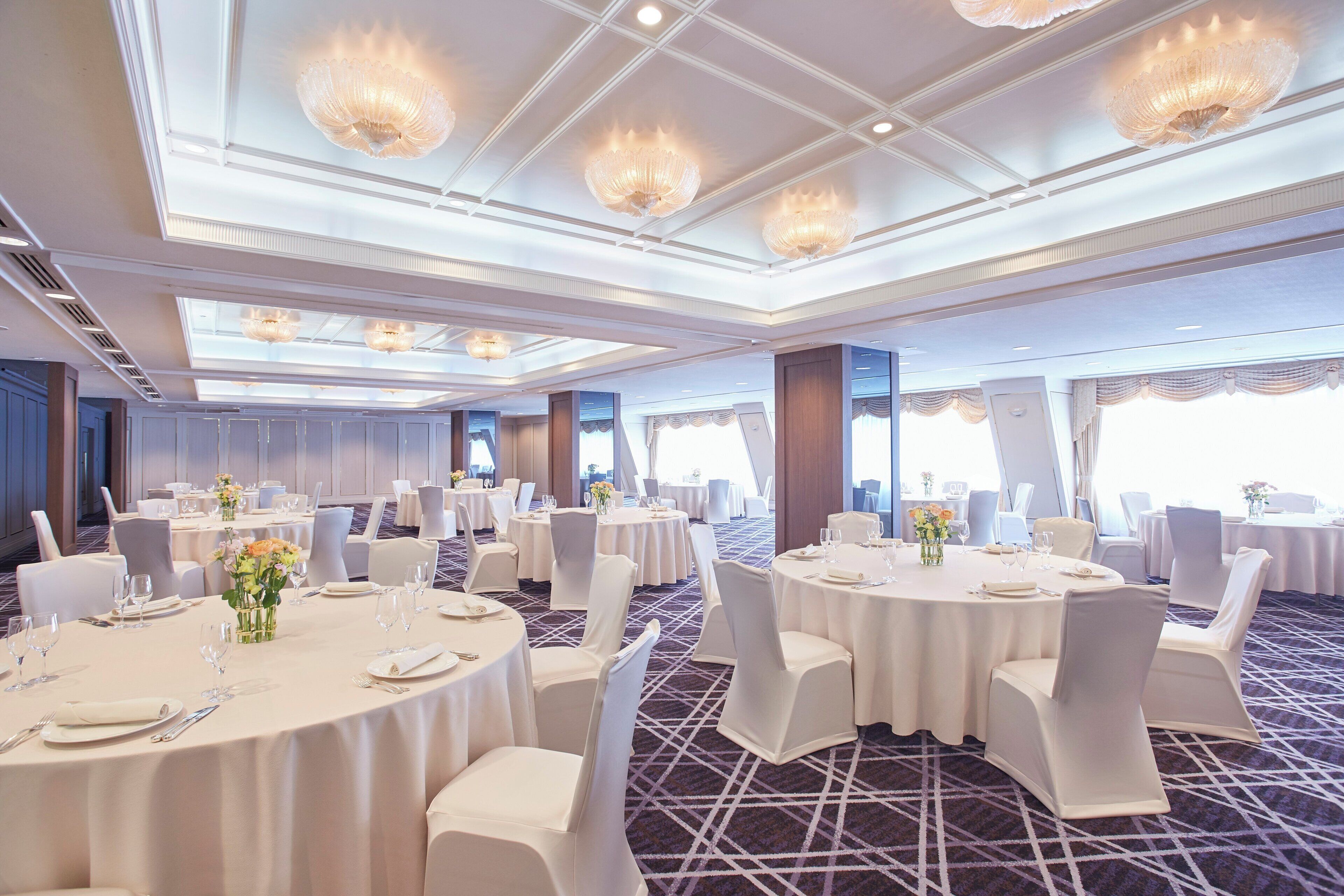 Een feestzaal met ronde tafels, witte stoelen en kroonluchters.