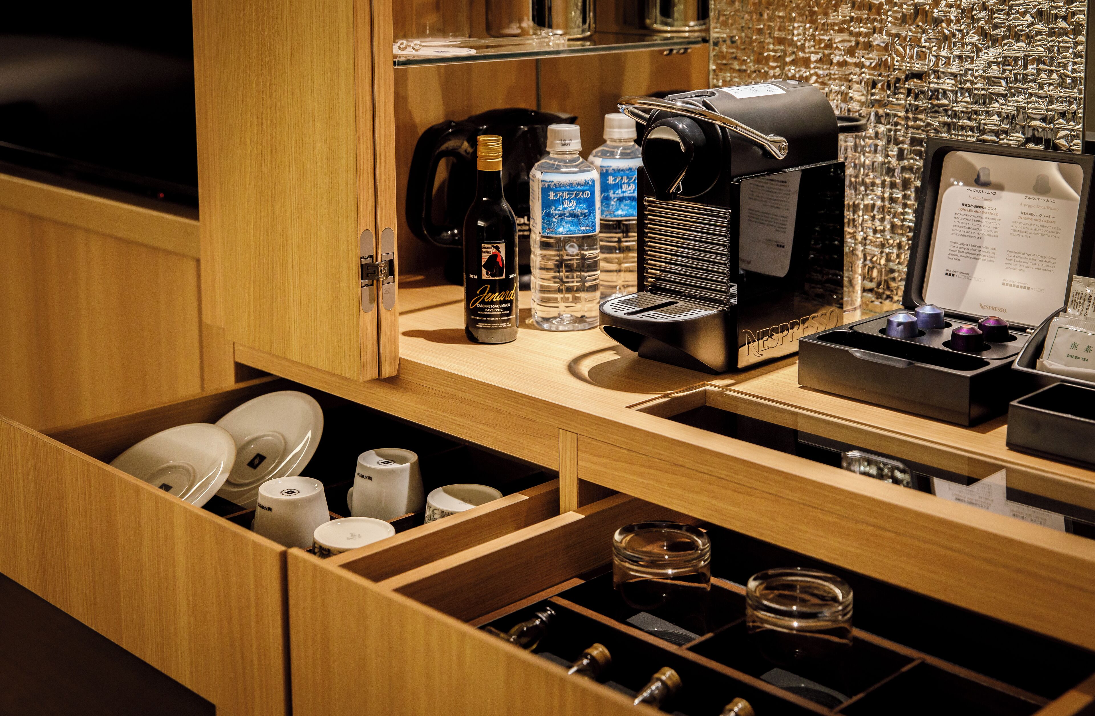 Un minibár bien organizado con una cafetera, agua embotellada y una botella de vino.