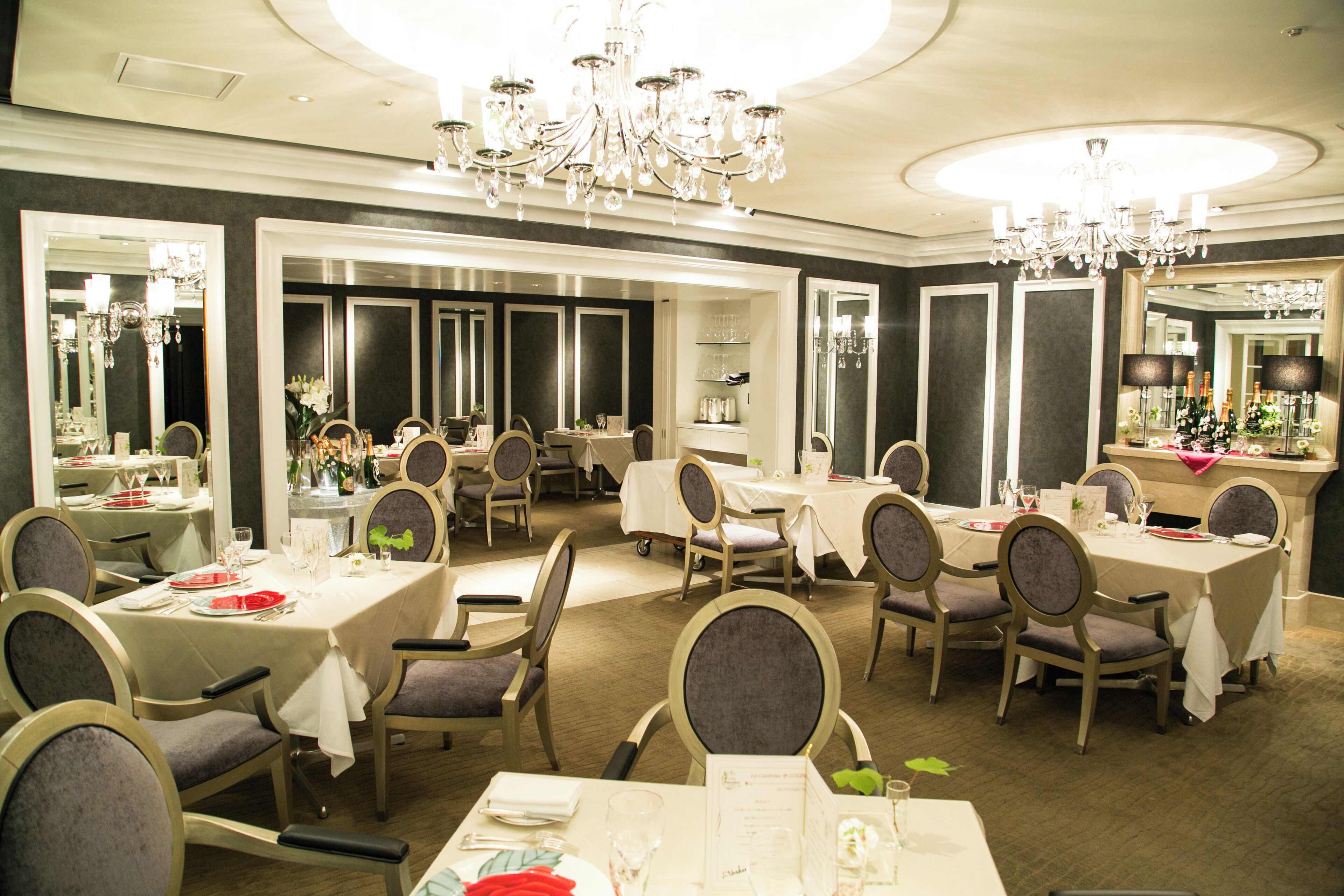 A formal dining area with multiple tables and chairs, chandeliers, and large mirrors.