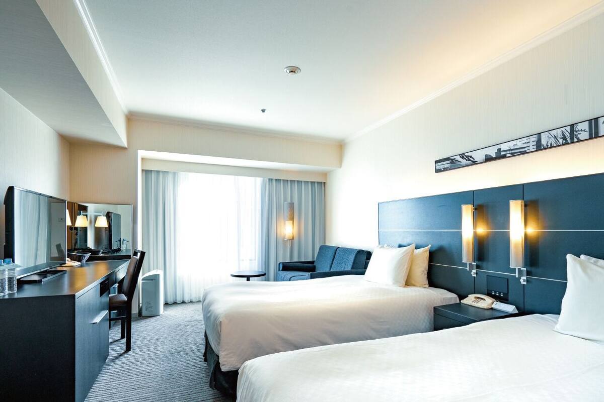 A hotel room with two beds, a desk with a chair, a small table, and a TV.