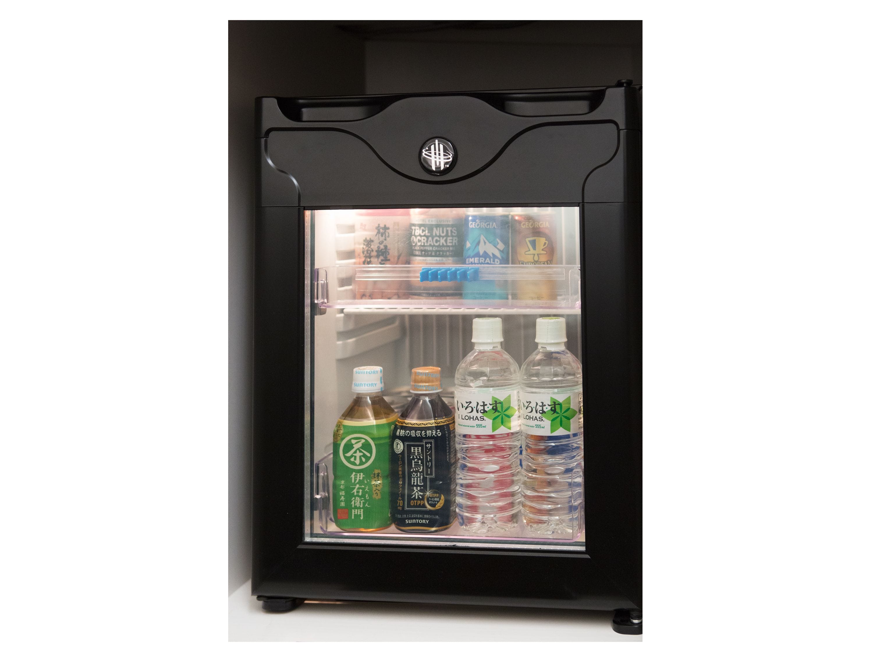Un refrigerador negro con puerta de vidrio, que contiene diversas bebidas y una botella azul de agua.