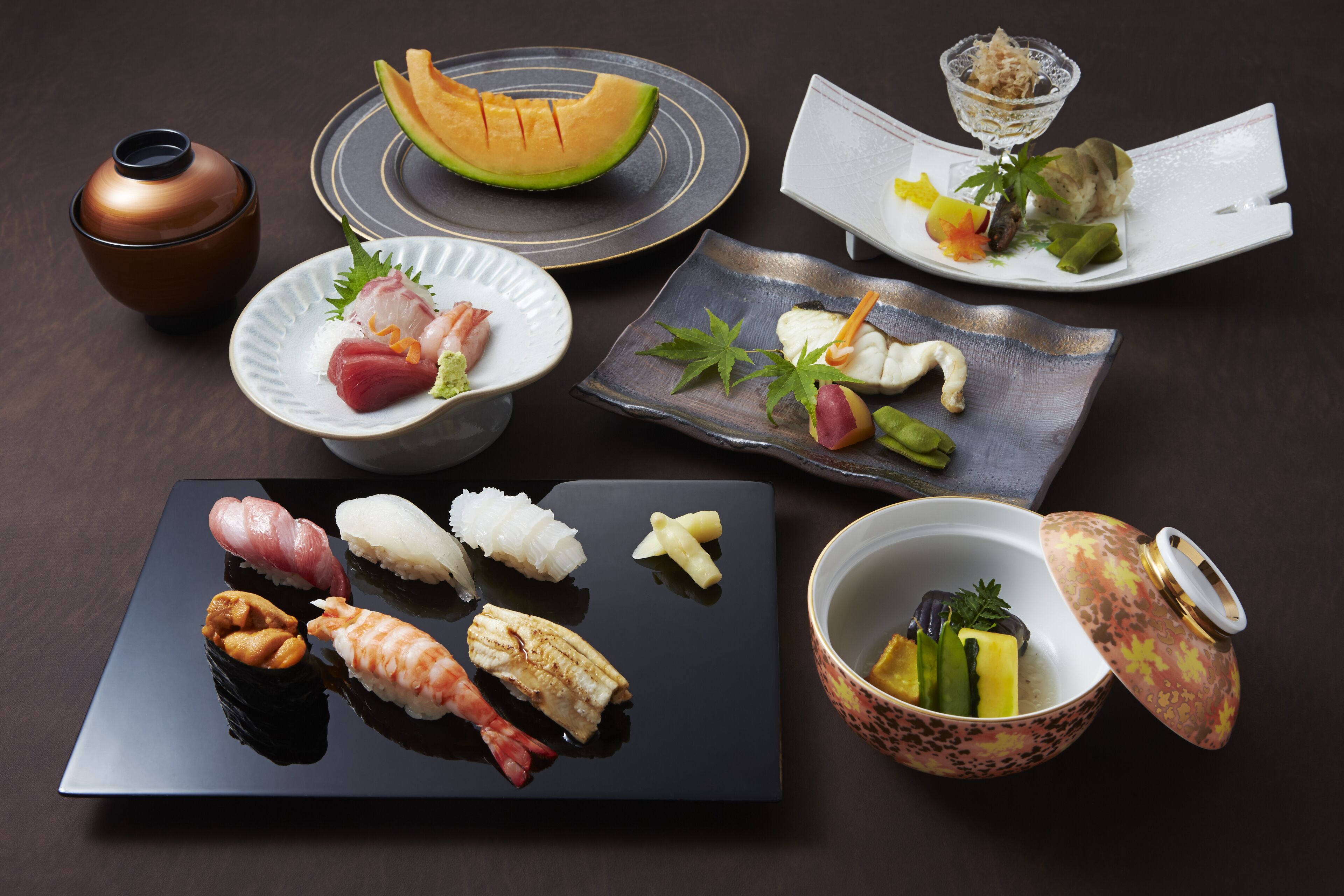 A variety of sushi dishes and a melon on a dark table.