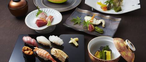 A variety of sushi dishes and a melon on a dark table.