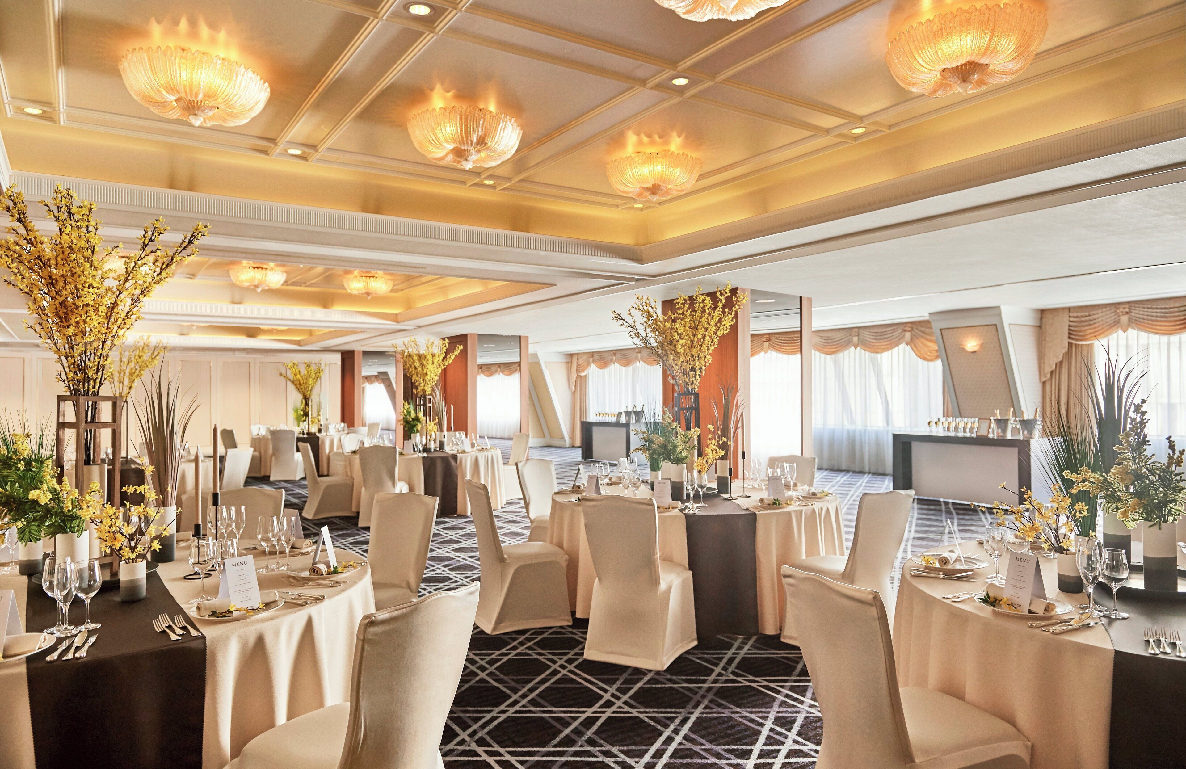 A banquet hall with round tables, chairs, and chandeliers.
