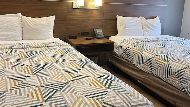 Een hotelkamer met twee bedden, elk voorzien van beddengoed met een patroon, een houten hoofdbord, bedlampen en een nachtkastje met een telefoon en een klein tafeltje.