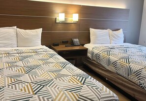 Una camera d'albergo con due letti, ognuno con biancheria a motivi decorativi, un poggiatesta in legno, lampade da comodino e un comodino con un telefono e un piccolo tavolo.