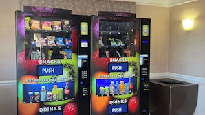 Twee automaten met snacks en drankjes, voorzien van aanduidingen 'SNACKS' en 'DRINKEN', en een 'DUW'-knop bij elk.