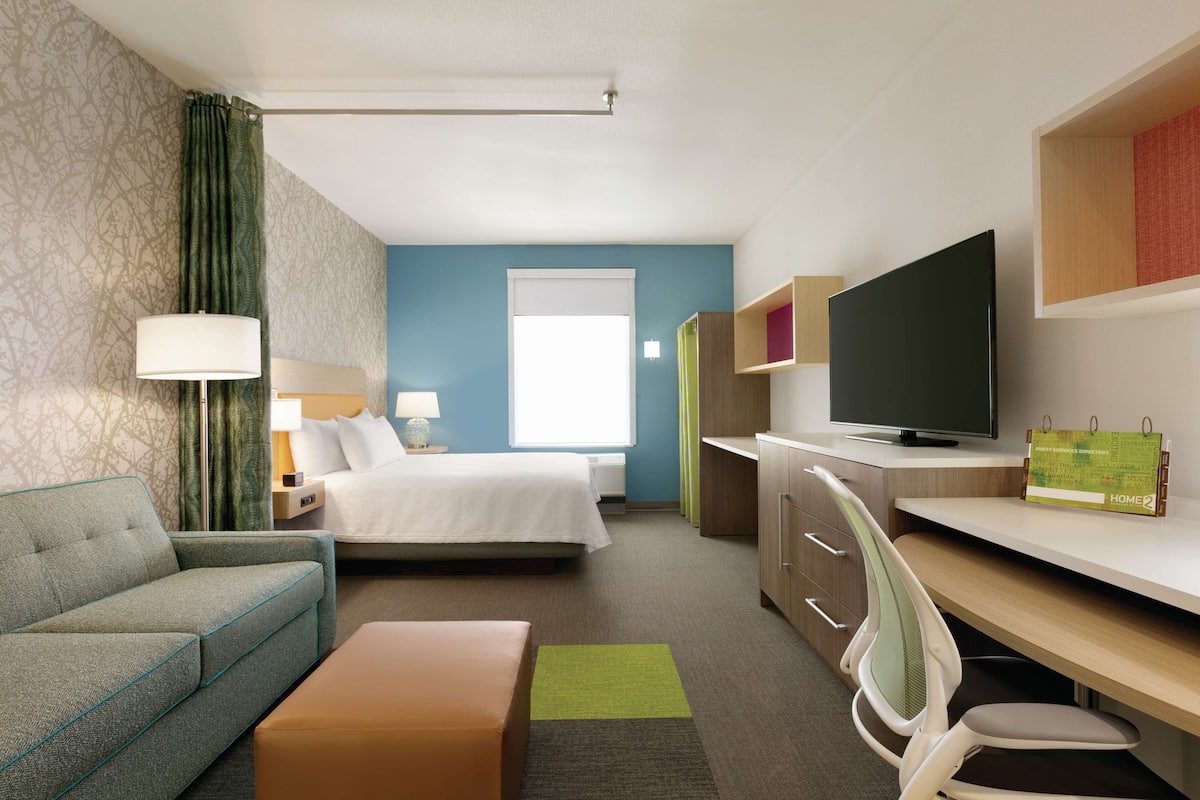 A hotel room with a bed, a sofa, a desk, a TV, and a calendar.
