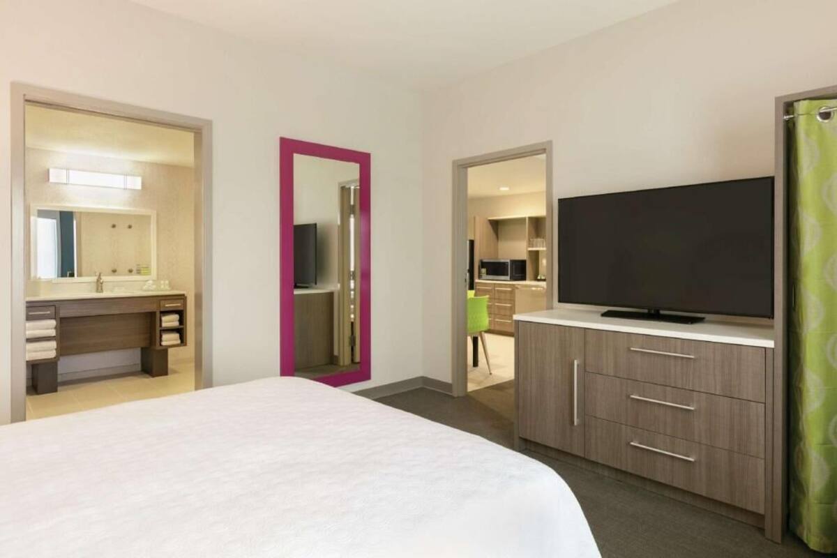 A hotel room with a bed, a TV, a bathroom, and a kitchenette.