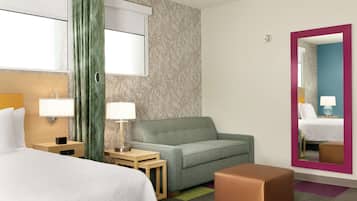 Una habitación de hotel con una cama, un sofá, una mesita con una lámpara, un espejo y una alfombra colorida.
