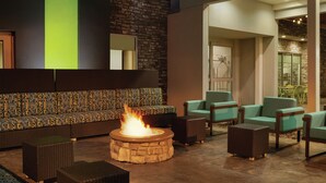 A lounge area with a stone fire pit, wicker furniture, and a stone wall. - Home2 Suites by Hilton Williamsville Buffalo Airport (Buffalo)