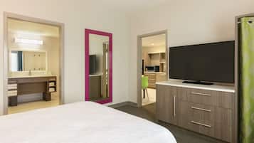 A hotel room with a bed, a TV, a bathroom with a mirror, and a kitchenette.