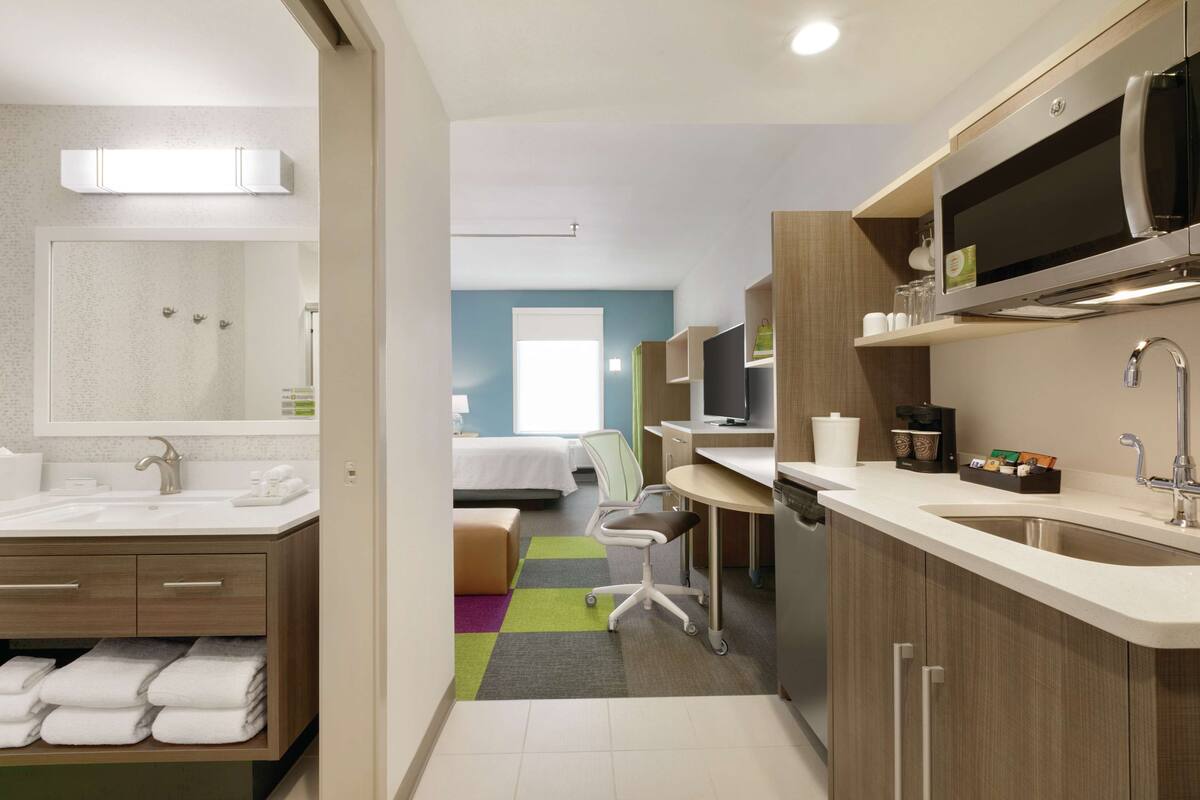 A modern hotel room with a bathroom, kitchenette, and a bed.