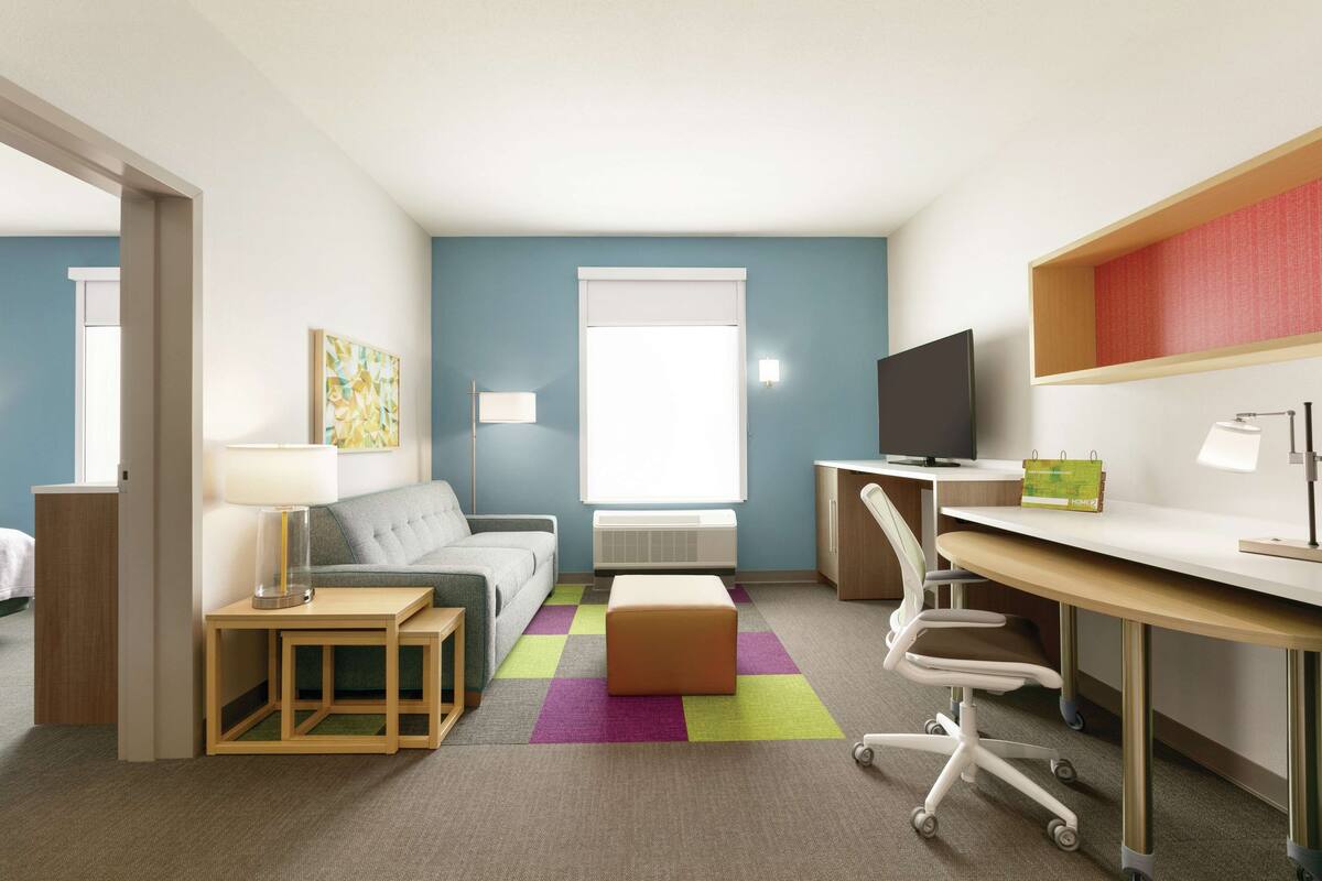 A modern hotel room with a sofa, a desk, a television, and a colorful rug.