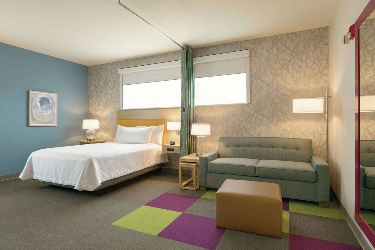 A hotel room with a bed, a sofa, a small table, and a chair.