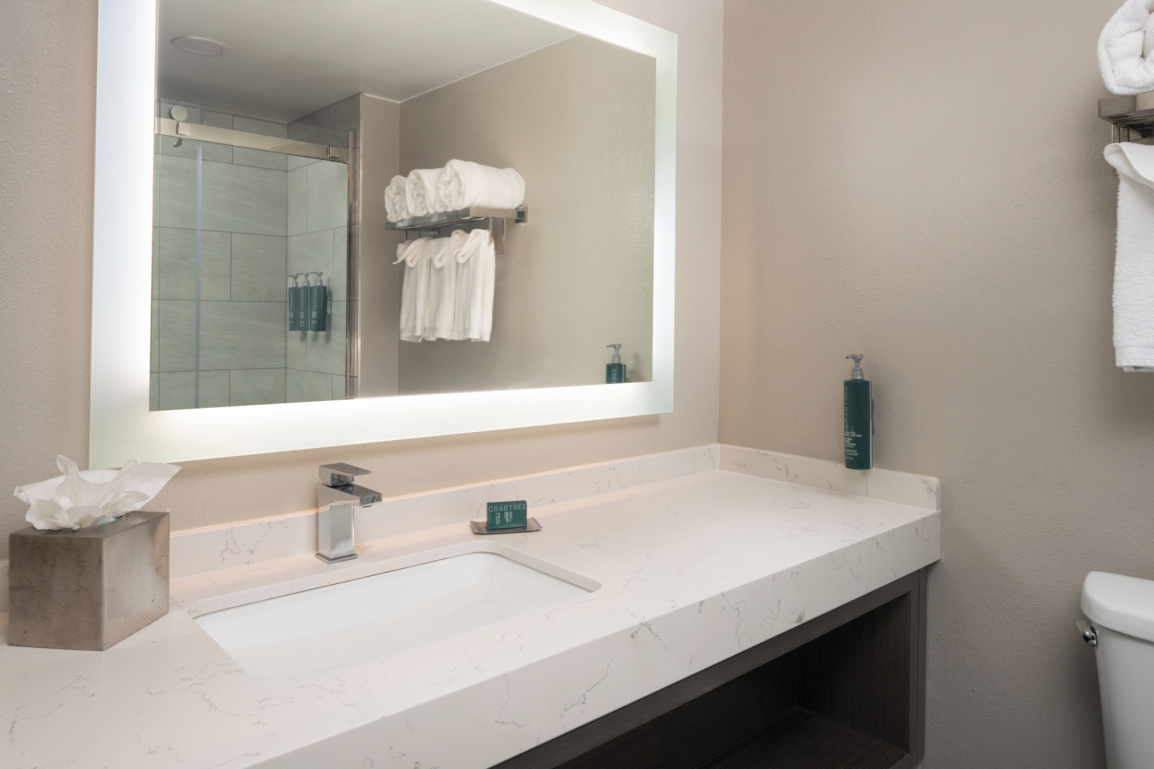 Une salle de bain avec un grand miroir, un lavabo en marbre, un porte-serviettes avec des serviettes pliées et des toilettes.