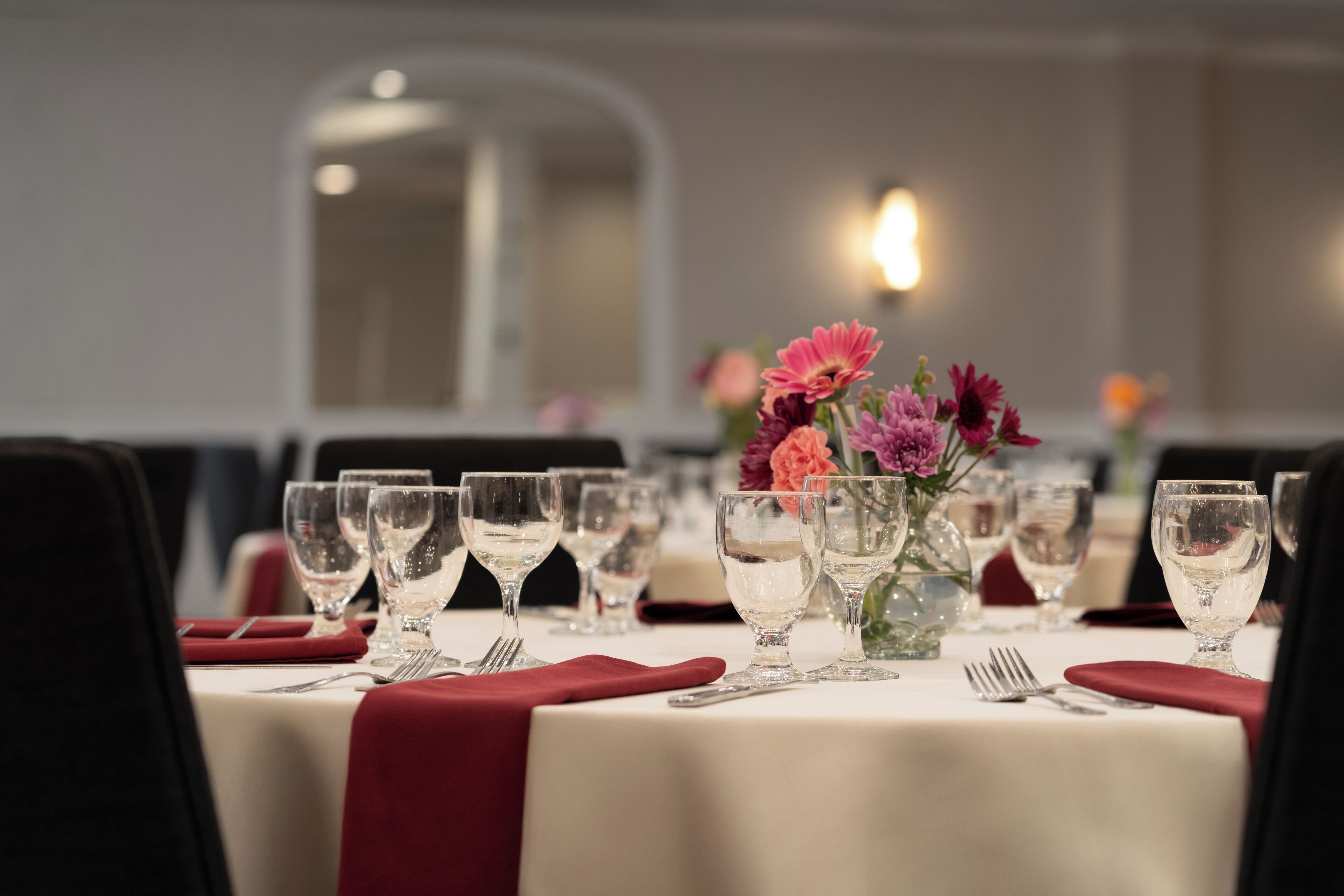 A dining table set with multiple wine glasses, a vase with flowers, and red napkins.