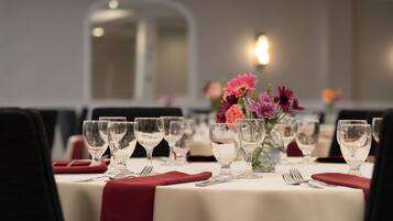 A dining table set with multiple wine glasses, a vase with flowers, and red napkins.