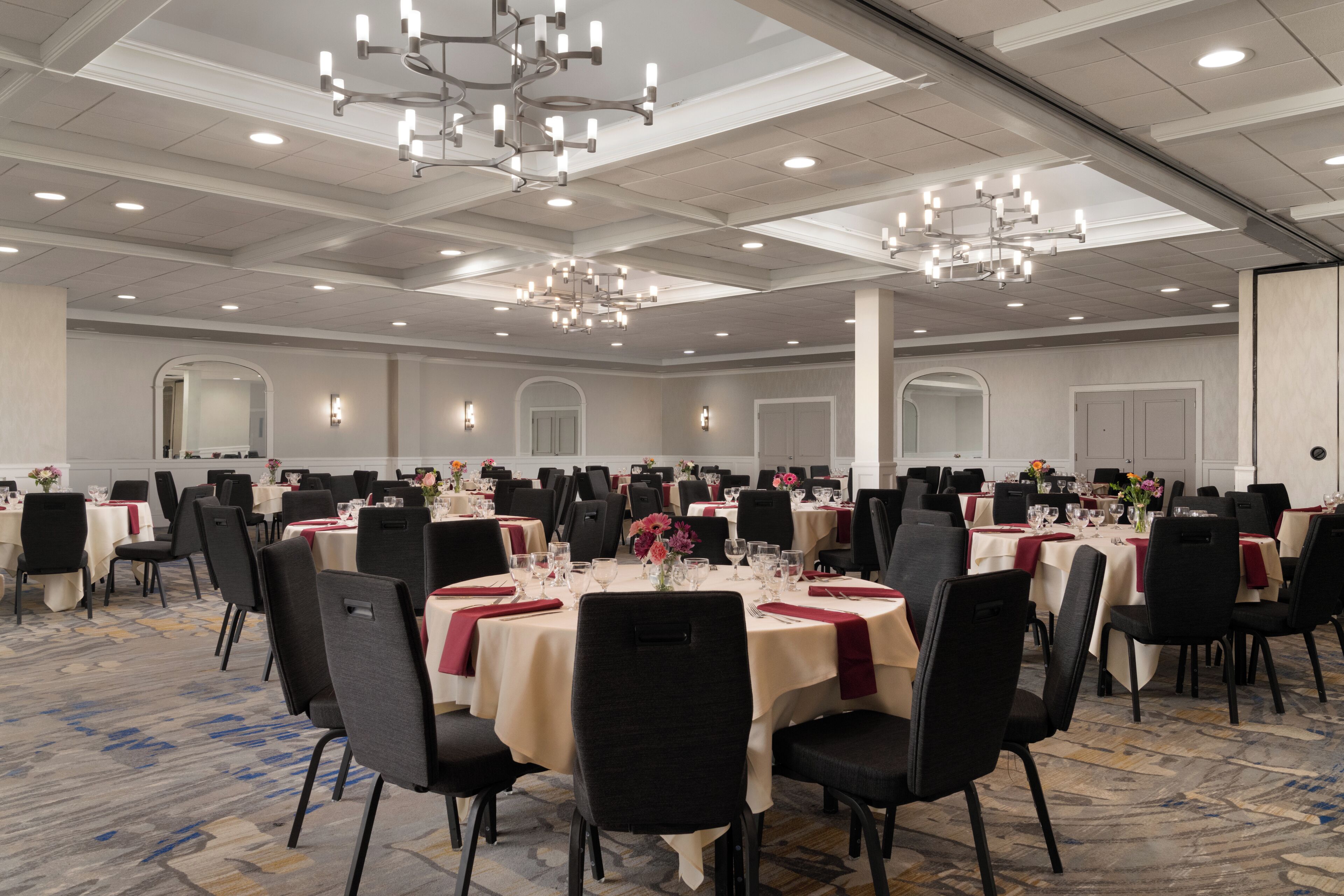 Un amplio salón de banquetes con mesas redondas, sillas negras y candelabros.