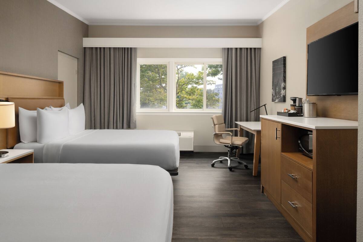 Une chambre d’hôtel avec deux lits, un bureau, une chaise, une télévision et une fenêtre avec des rideaux.