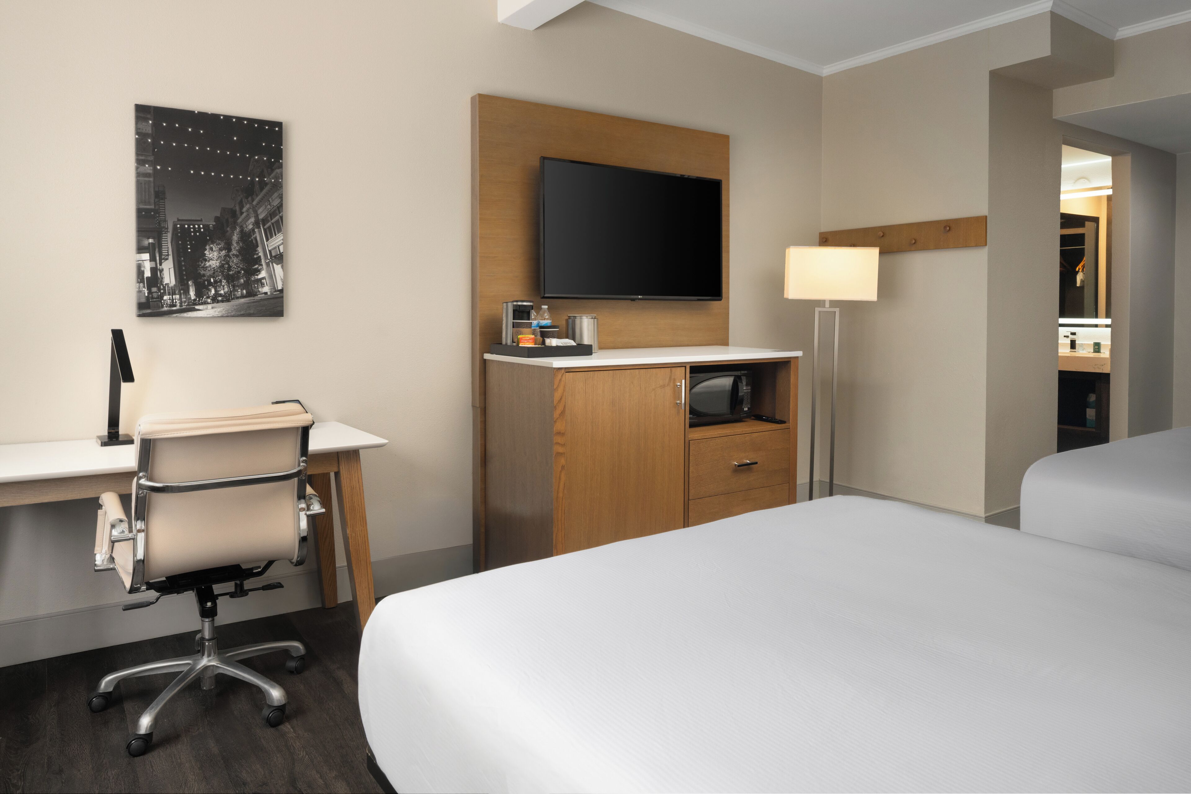 A hotel room with a bed, a desk with a chair, a flat-screen TV, a lamp, and a mirror.