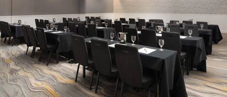 A conference room with rows of tables and chairs, equipped with water pitchers and wine glasses.