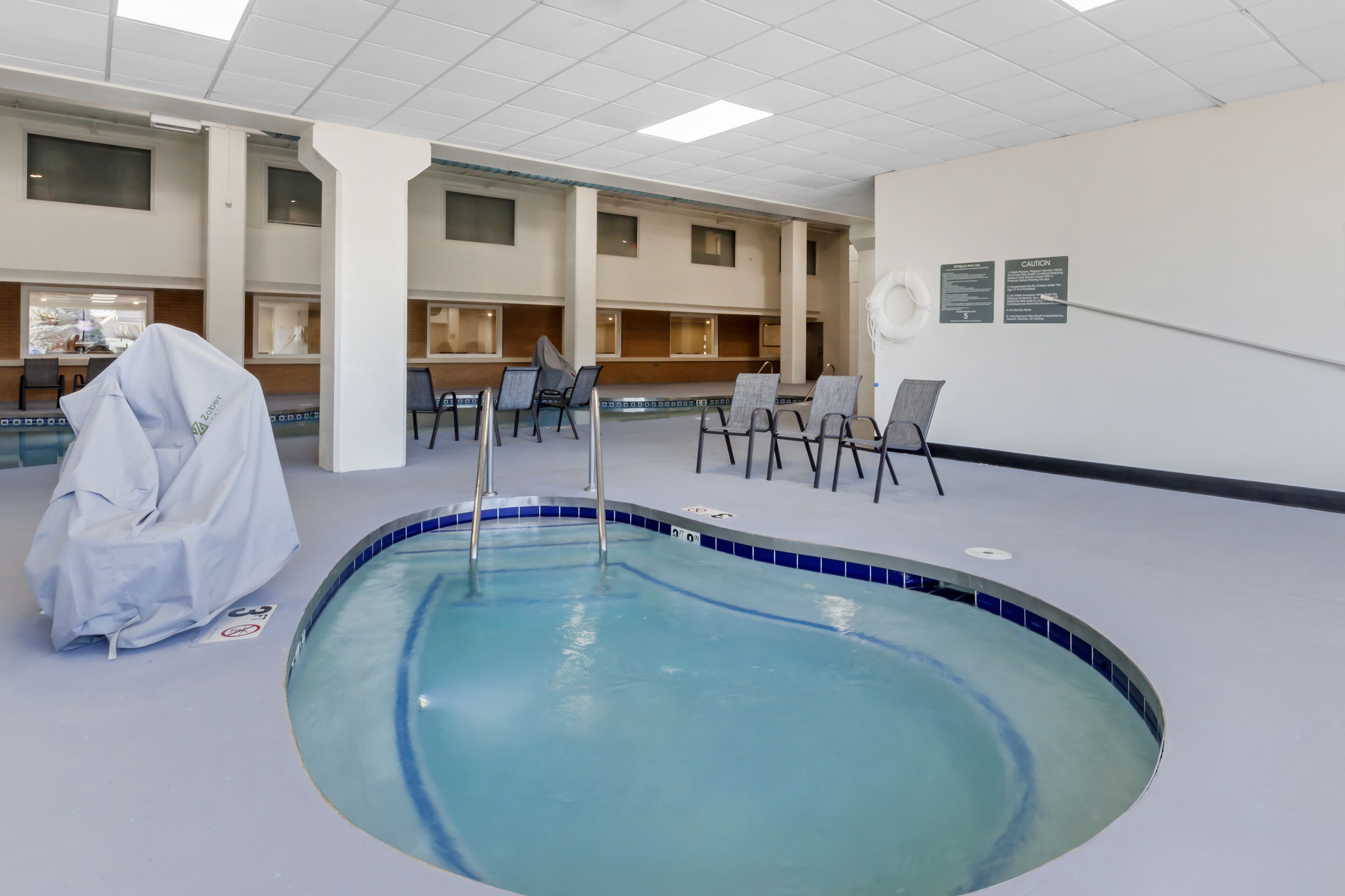 Une piscine intérieure dont le bord est recouvert de carreaux bleus, entourée de chaises et de tables.