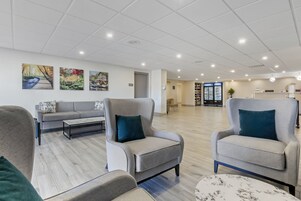 Um hall amplo com um sofá cinzento, duas poltronas, uma mesa de centro e uma estante de livros.