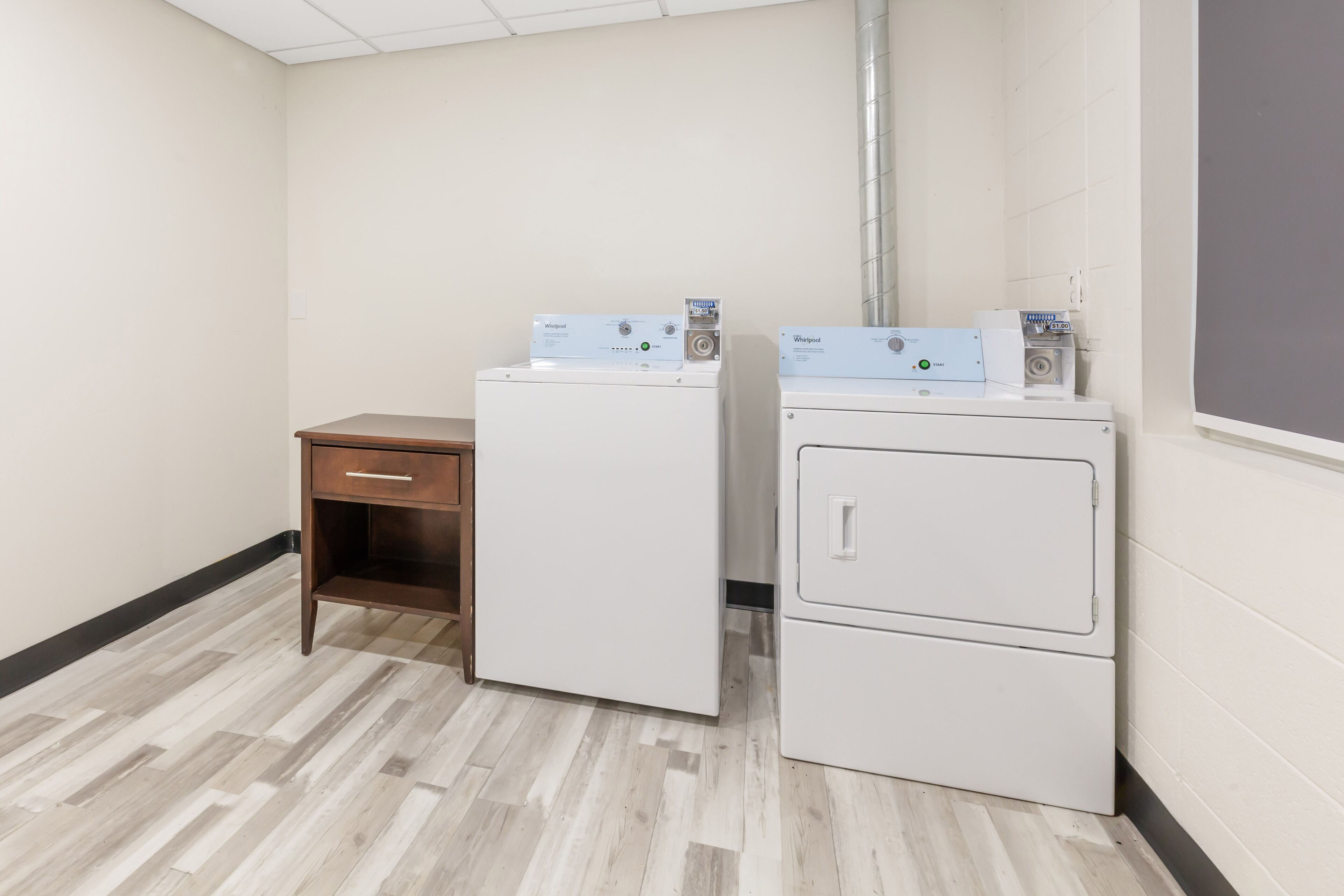 A laundry room with two stacked washers and dryers, a wooden cabinet, and a white wall.