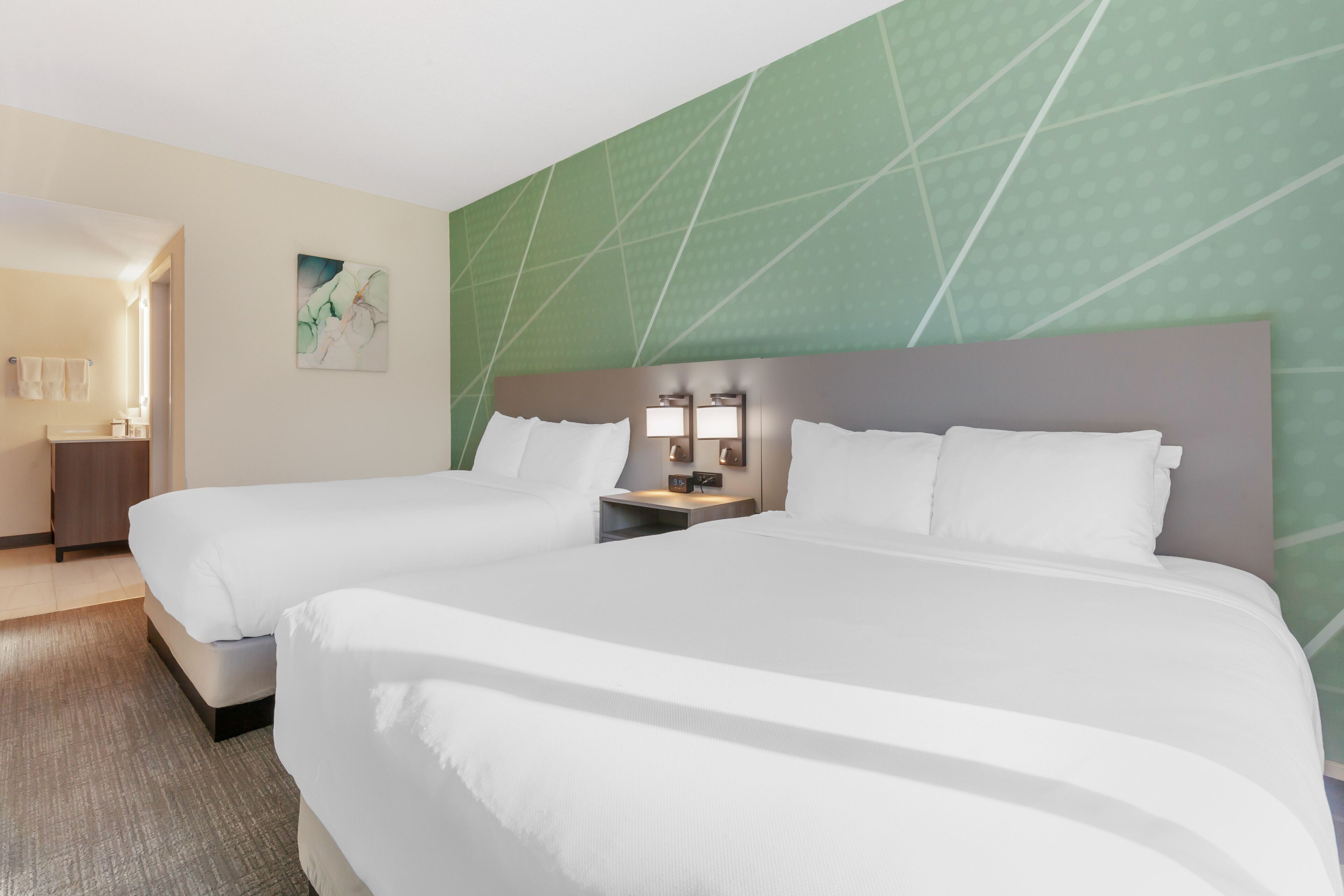 Une chambre d’hôtel avec deux lits, une table de chevet avec une lampe et un mur orné d’un motif vert.