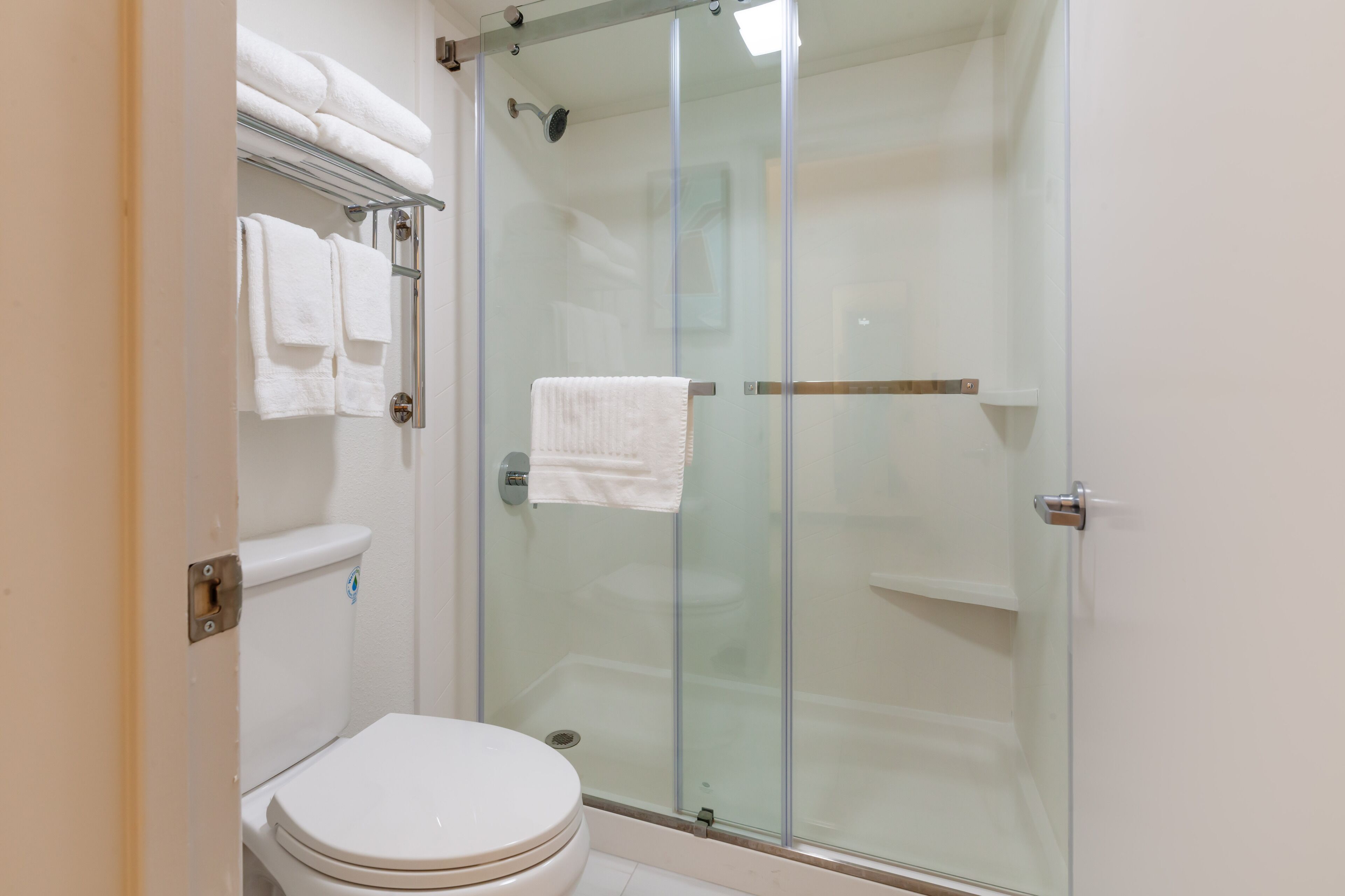 A bathroom with a glass-enclosed shower, a toilet, and a towel rack with folded towels.