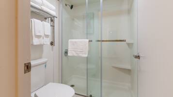 A bathroom with a glass-enclosed shower, a toilet, and a towel rack with folded towels.