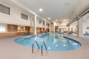 Piscina interna com água cristalina, rodeada por espreguiçadeiras e um piso ladrilhado.